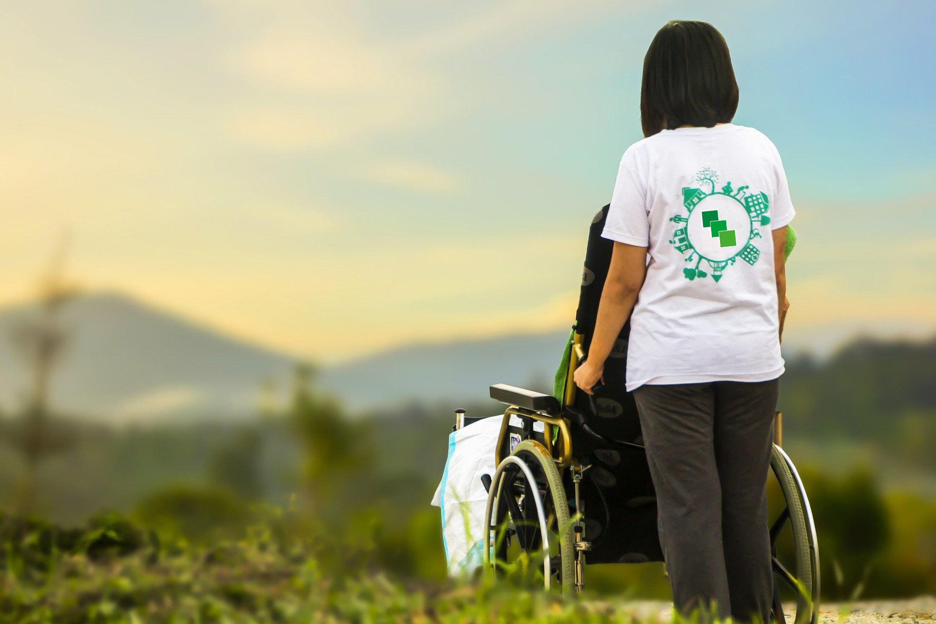 Pflegerin mit Patientin im Rollstuhl im freien, Berge und Grün